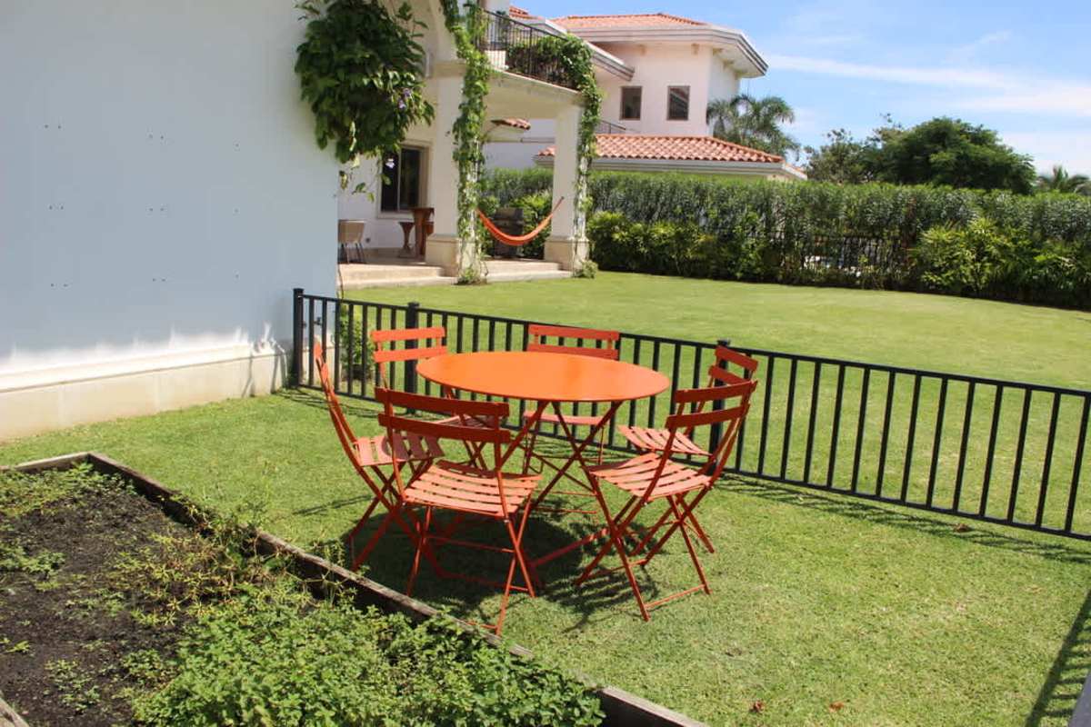 Backyard patio with orange dining set, green lawn and garden beds Santa María Golf & Country Panama