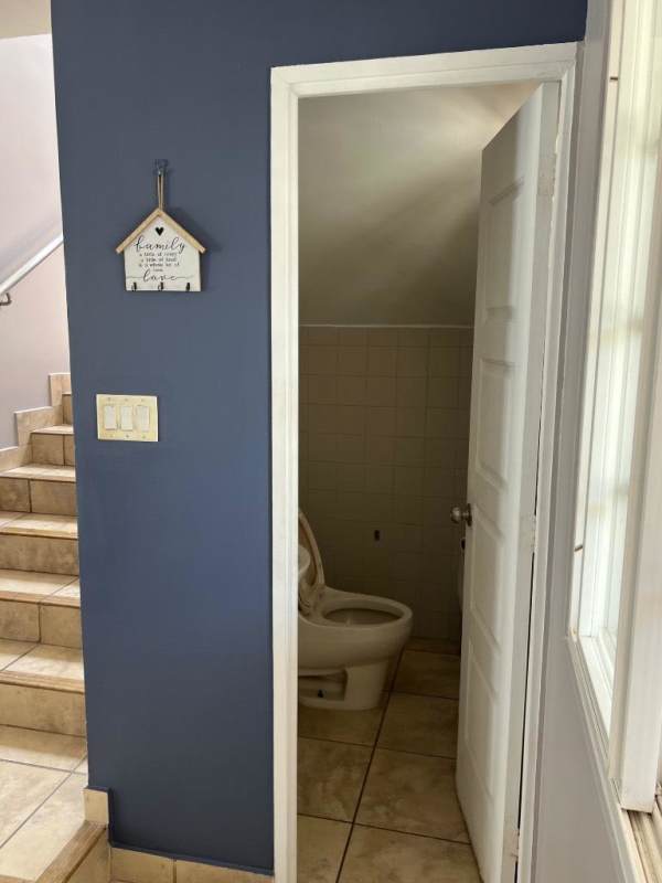 Guest half bathroom under stairs with blue wall, toilet, and ceramic flooring at PH Everest Panama