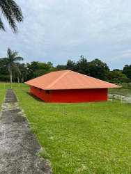 Small bright red building with orange hipped roof in grassy yard with palms and fence in Panama countryside
