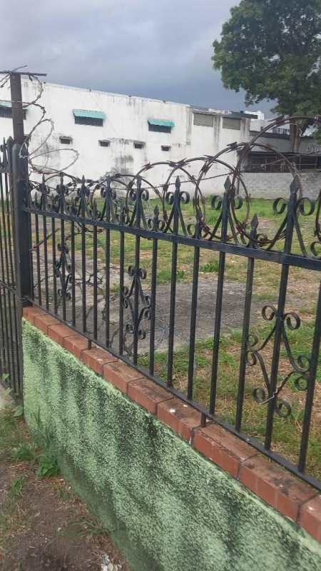 Fenced vacant lot with brick base and security barbed wire near white building Panama City