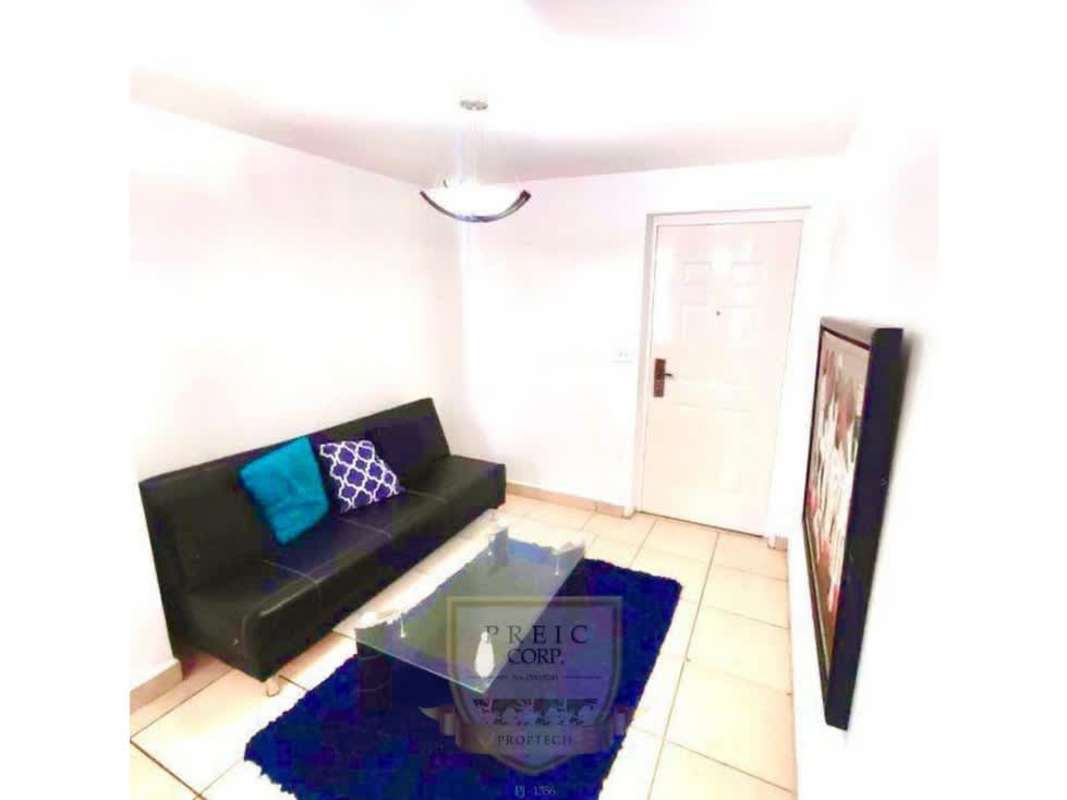 Living room with sofa, glass coffee table, tiled floor, and blue accents in furnished apartment PH Brisas de España Carrasquilla