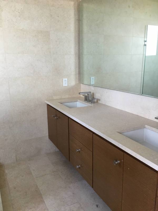 Bathroom with double sink vanity, large mirror, beige stone tiles in luxury condo Oceana Golf Panama