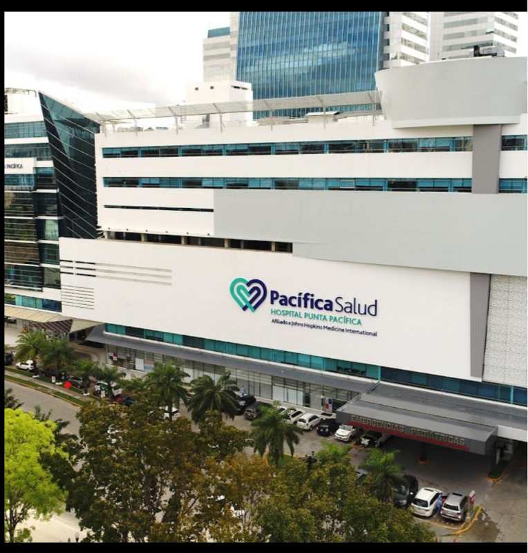 Exterior view modern glass high-rise PH Pacifica Salud connected to Hospital Punta Pacifica with palm trees and parking