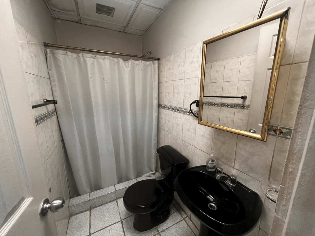 Bathroom with black sink, toilet, gold mirror frame, tiled walls commercial rental Panama