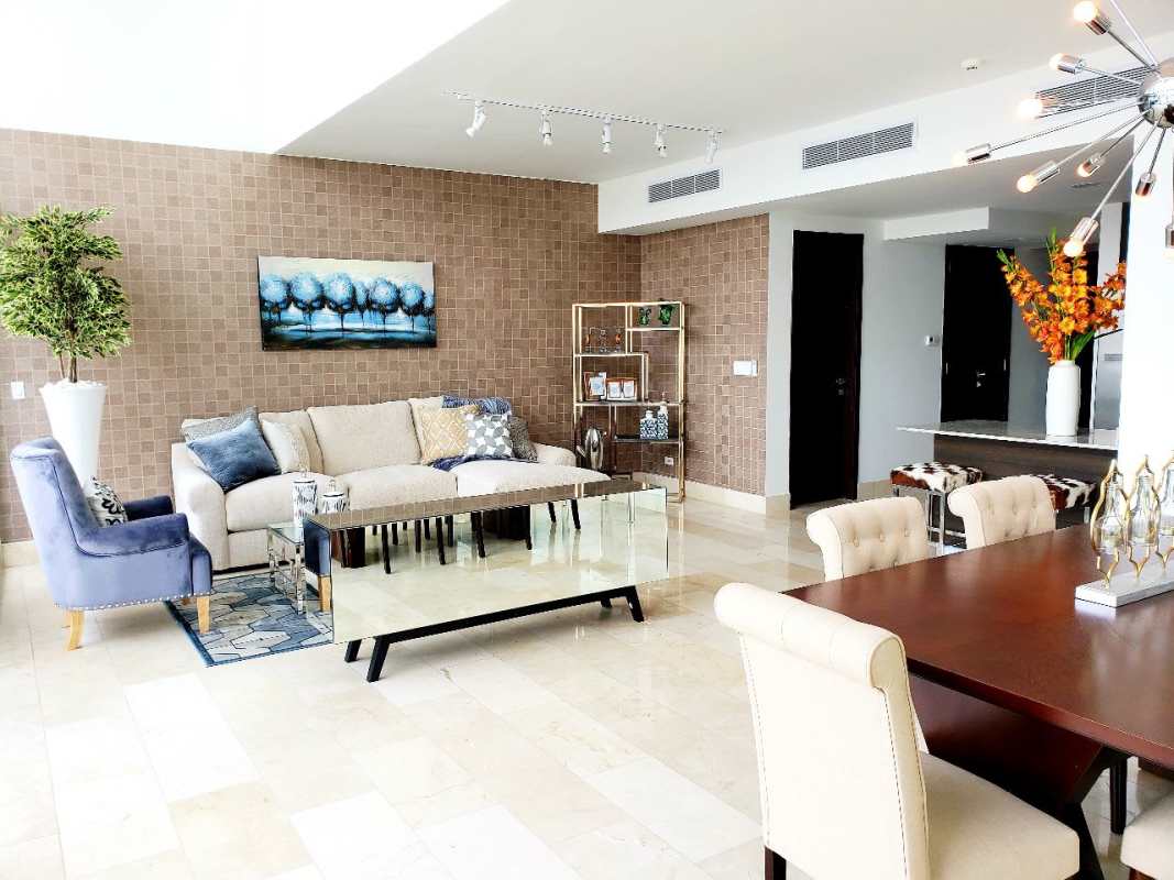 Bright open living-dining room with sectional sofa, blue accent chair, ocean view balcony access in Grand Tower Punta Pacifica