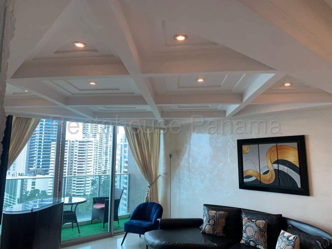 Living room with sofa, large windows, balcony access overlooking ocean