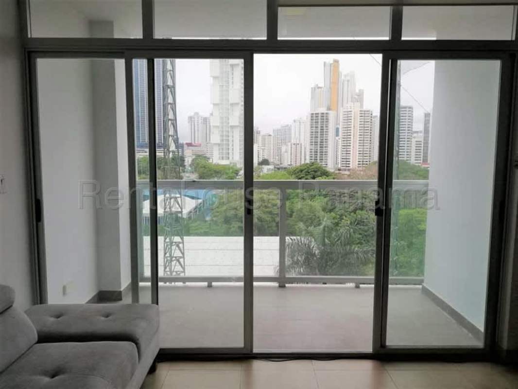 Bright living room with sliding glass doors, balcony access, and city skyline view at The One Tower Panama