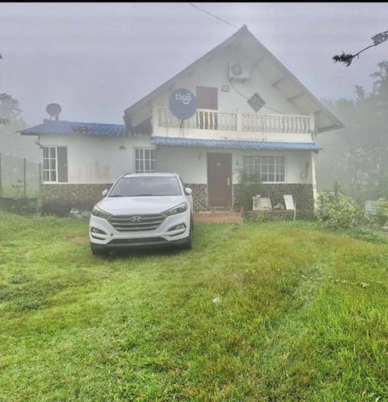 Two-story rustic house with balcony, blue roof, stone accents and foggy countryside backdrop in Cerro Viento Panama