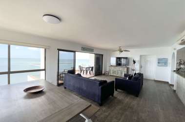 Modern coastal living room with ocean view balcony, navy sofas, ceiling fan in PH Malibu Tower beach condo Panama