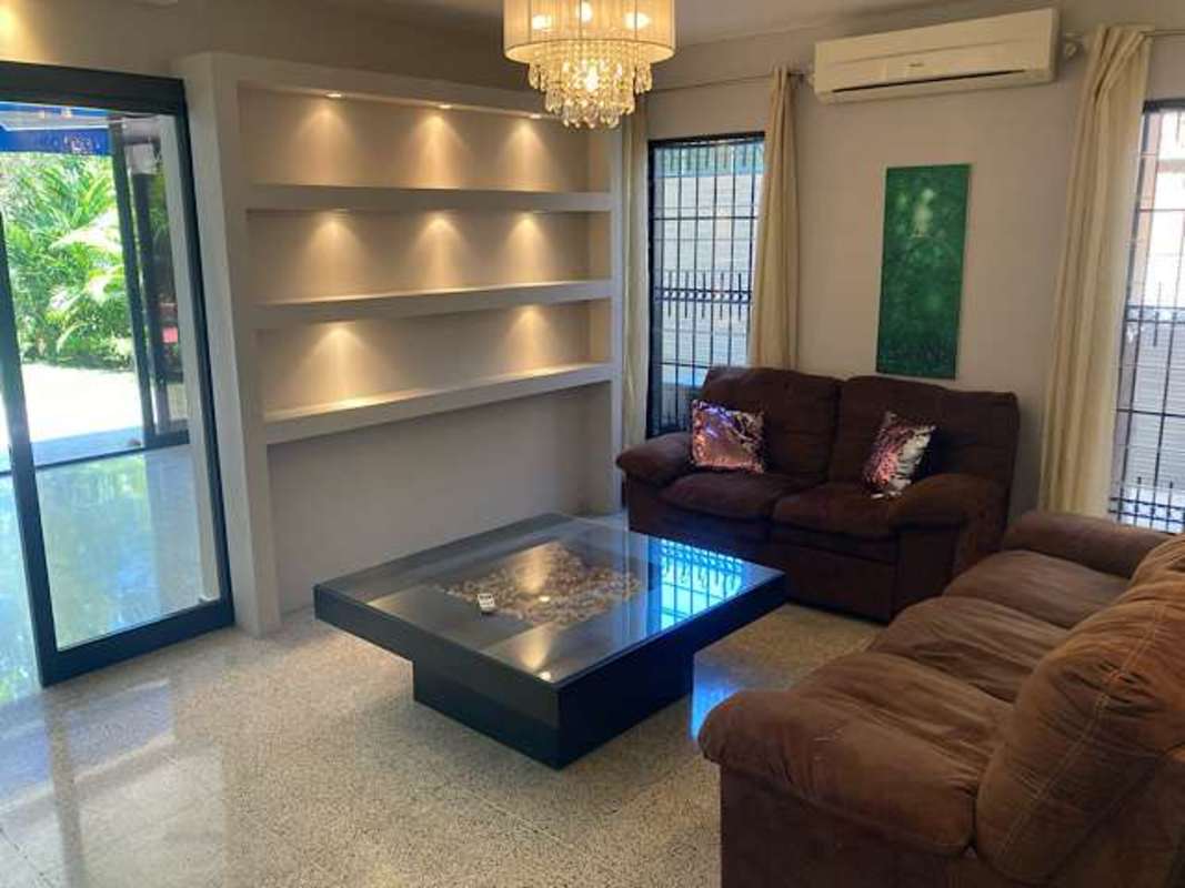 Bright living room with brown sectional sofa illuminated shelves chandelier and garden view in Panama house