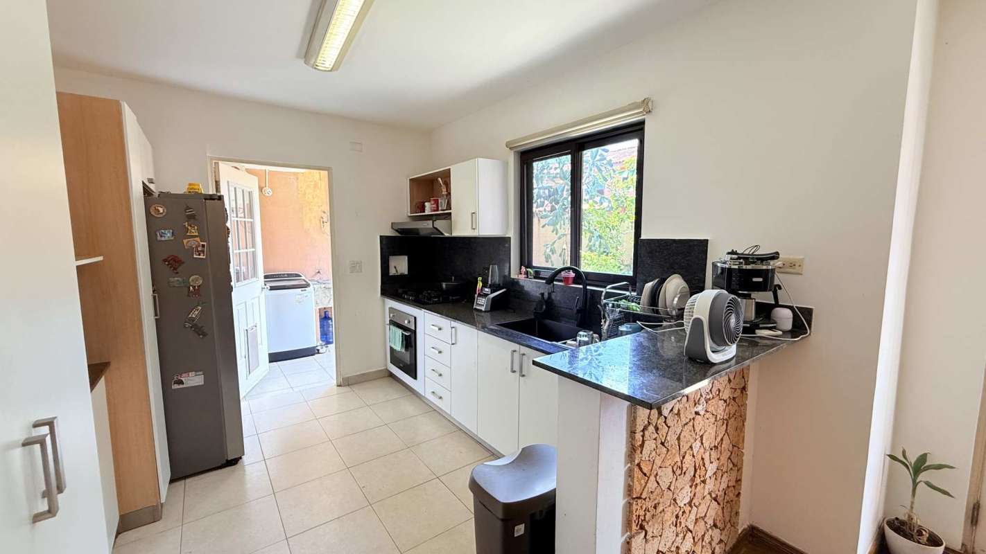 Kitchen with granite countertops, white cabinetry, and window in Versalles Costa Sur house
