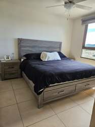 Modern bedroom with queen bed, ceiling fan, large window in furnished Panama Pacifico apartment