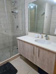 Bathroom with beige tiles, glass shower enclosure, vanity storage in furnished apartment Panama Pacifico