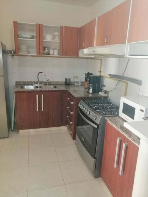 L-shaped kitchen with granite countertops, gas stove, overhead cabinets, microwave and refrigerator in Cerro Viento Panama