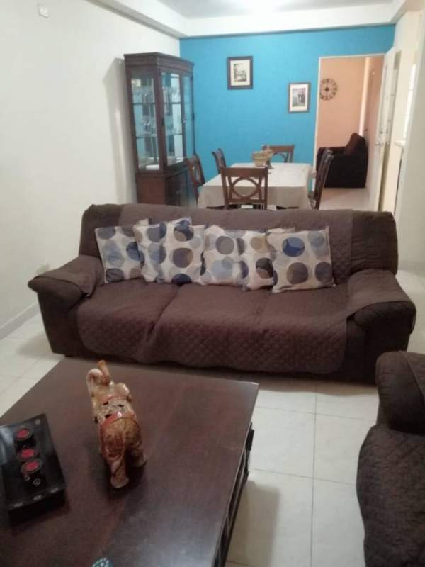 Open living dining area with brown sofas, blue accent wall, wood dining table, and glass cabinet in Colinas de Cerro Viento Panama