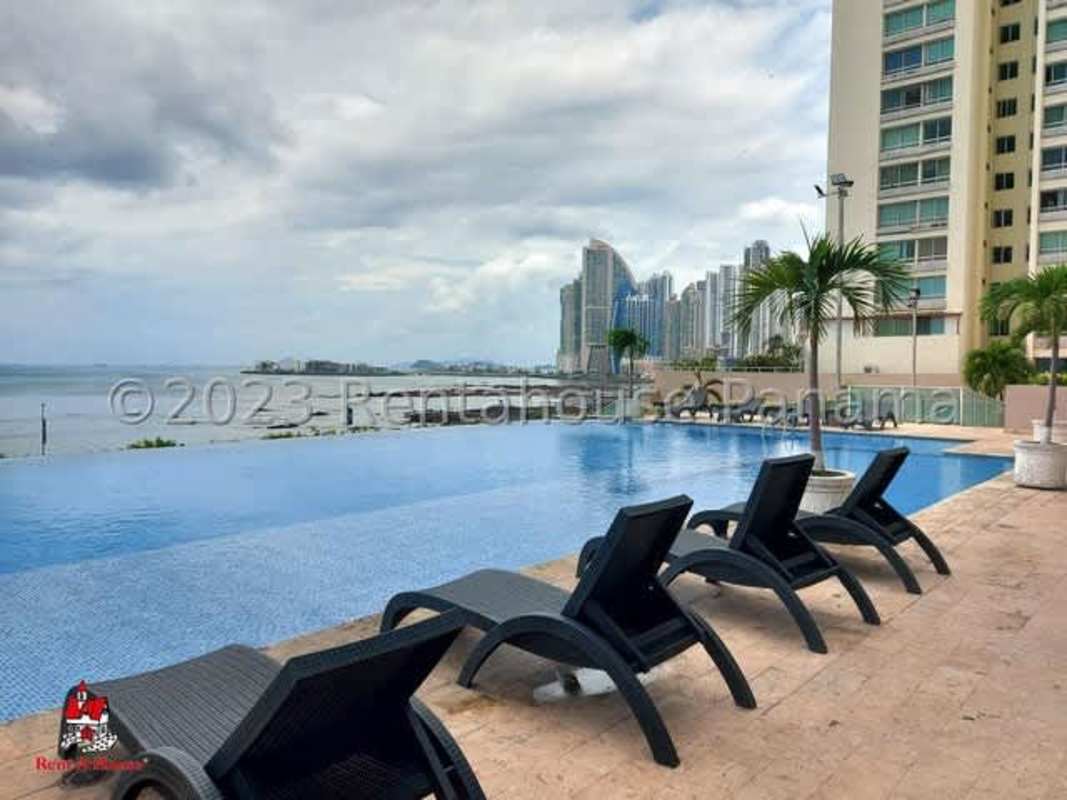 Infinity pool with black lounge chairs, view of city skyline and ocean at PH Terramar Panama City