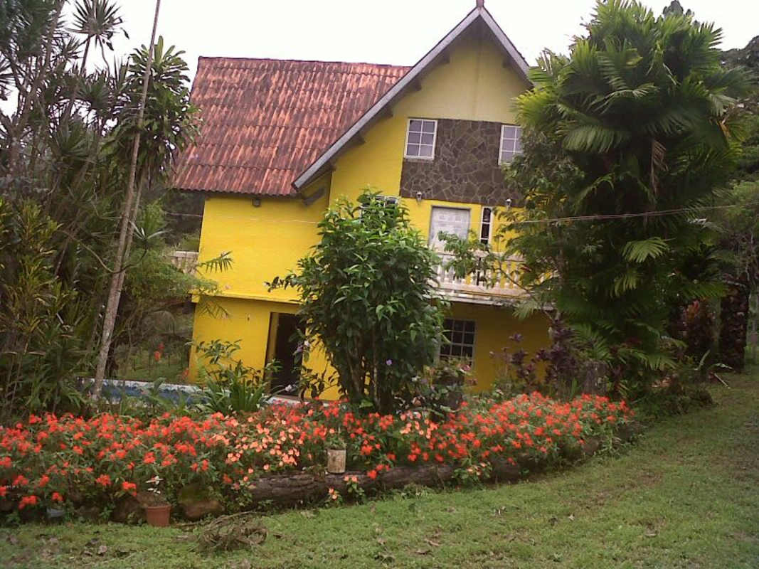 Rustic yellow two-story cottage with tiled roof, balcony, and lush garden with flowers in Cerro Azul Panama