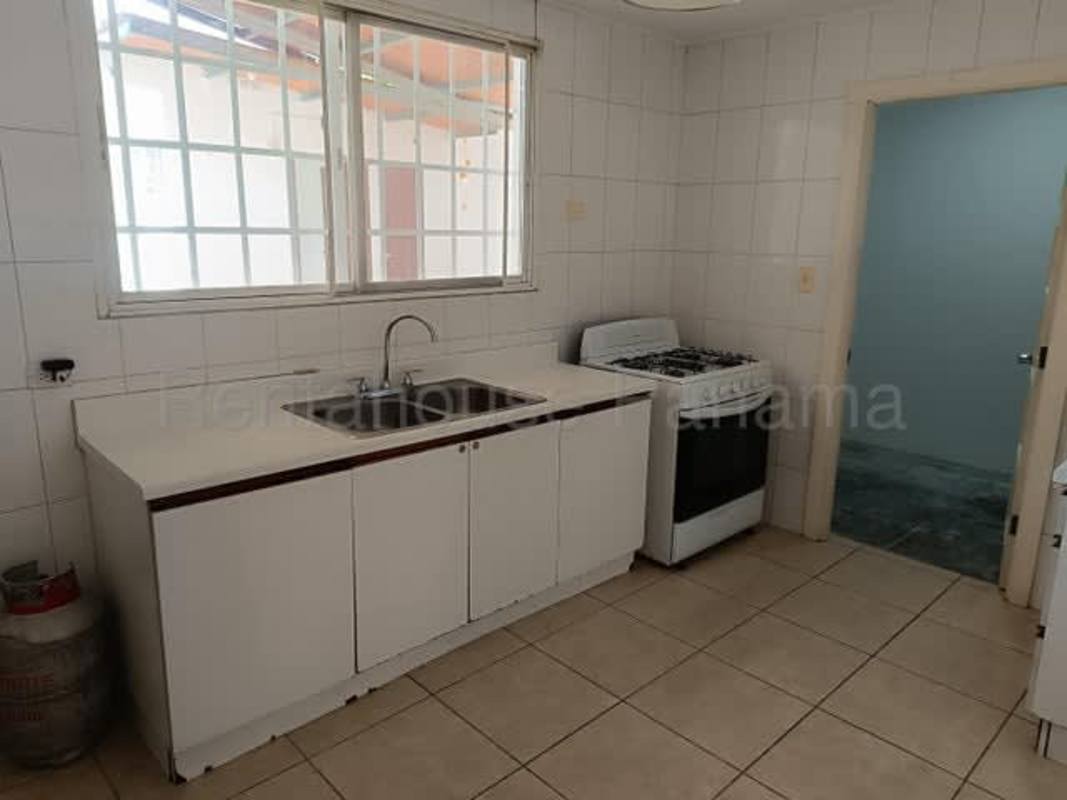 Kitchen area with window, white tiled walls, cabinets and gas stove in Brisas del Golf house Panama