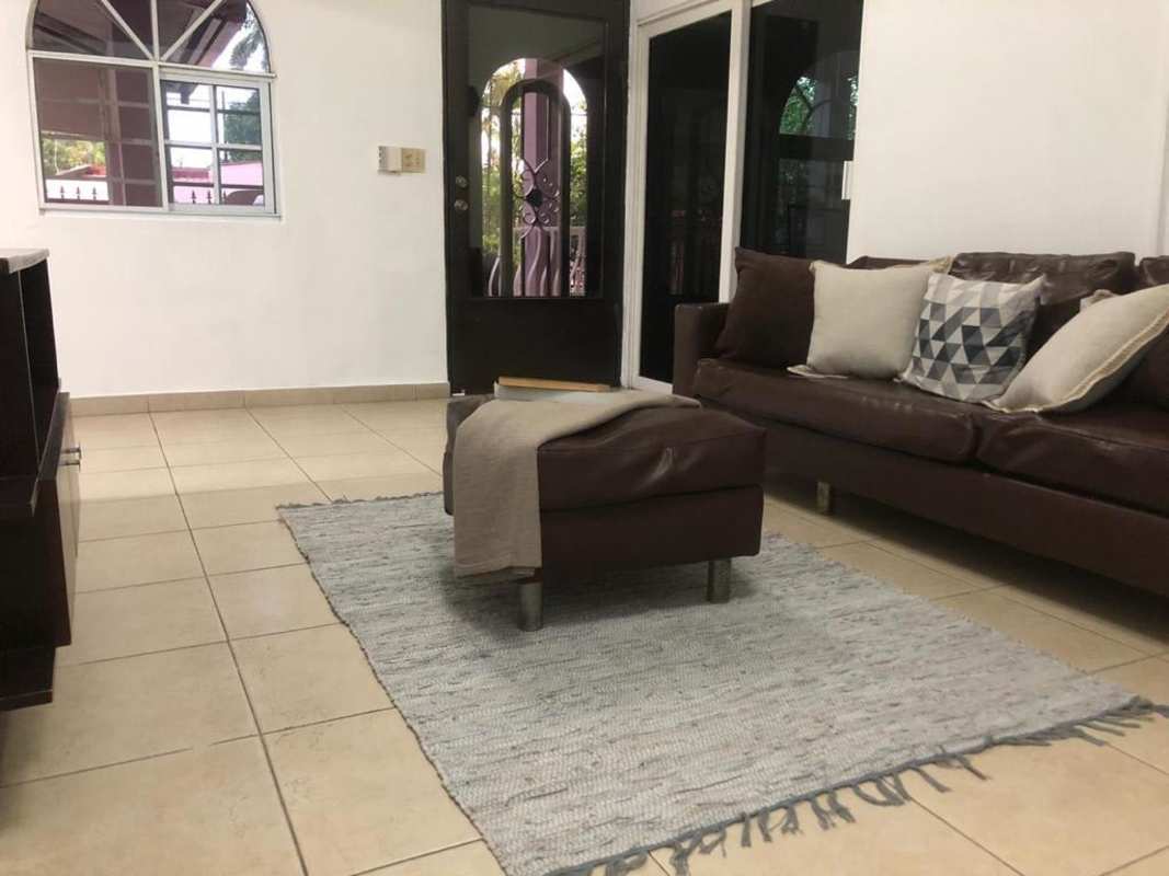 Living area with brown sofa, ottoman, tiled floor and terrace access at Villa Cáceres Panama