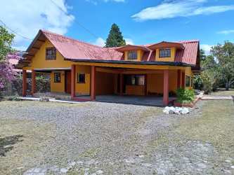 Exterior of rustic yellow two-story house with carport, dormer windows, red roof in Volcán