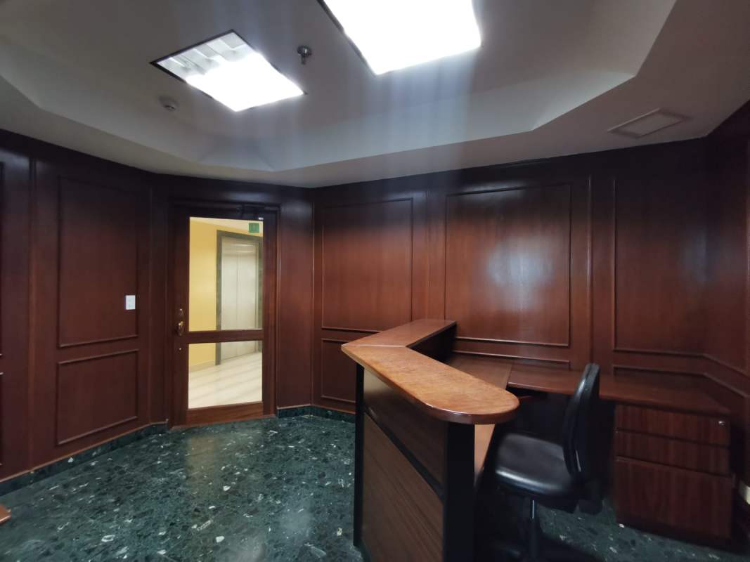 Reception lobby with wood panel wall, dark marble floor, and wooden desk in World Trade Center Marbella