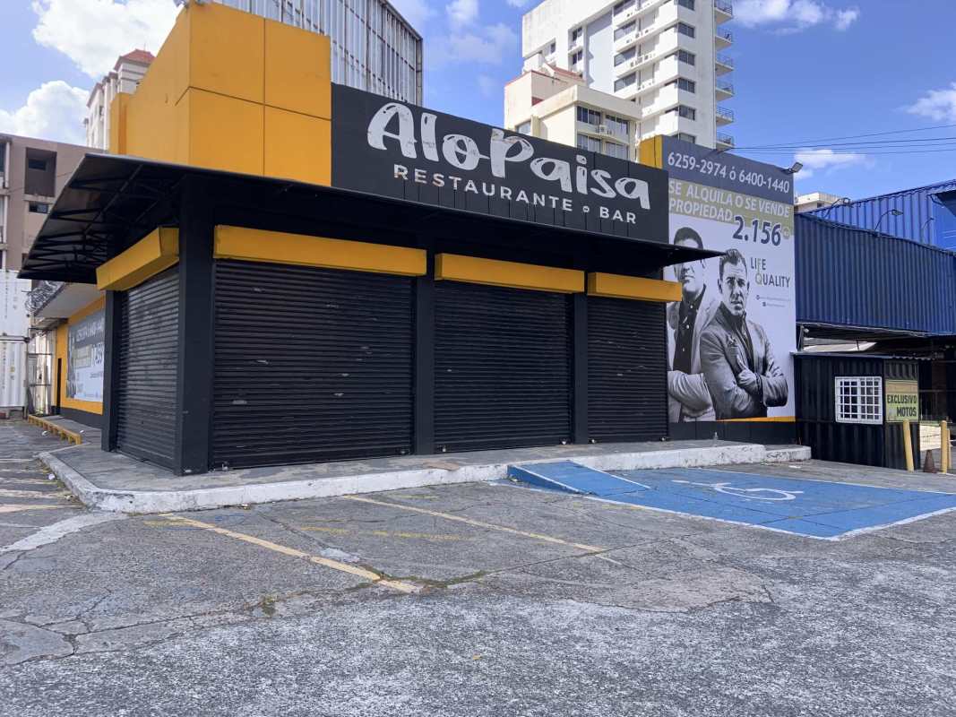 Corner commercial space with yellow and black restaurant facade, billboard, and parking on Via España in Panama City