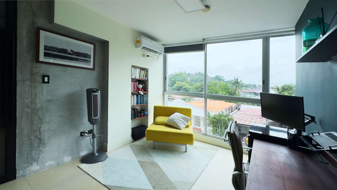 Modern home office with large windows, yellow chair, concrete accent wall in PH Novoa Villa Cáceres Panama