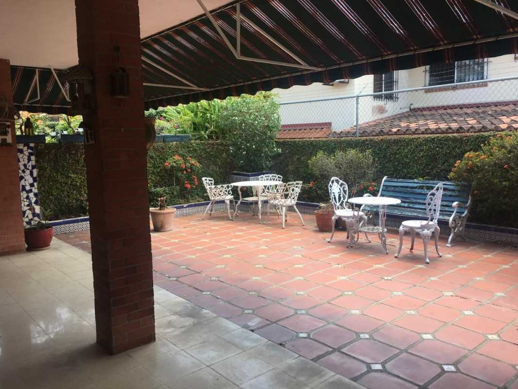 Mediterranean-inspired covered patio with striped awning, terracotta tiles and hedged fence in La Alameda house Panama City.