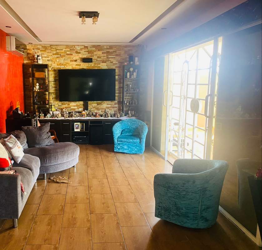 Contemporary living room with accent wall, large TV, grey sofa, teal chairs in house Brisas del Golf Panama