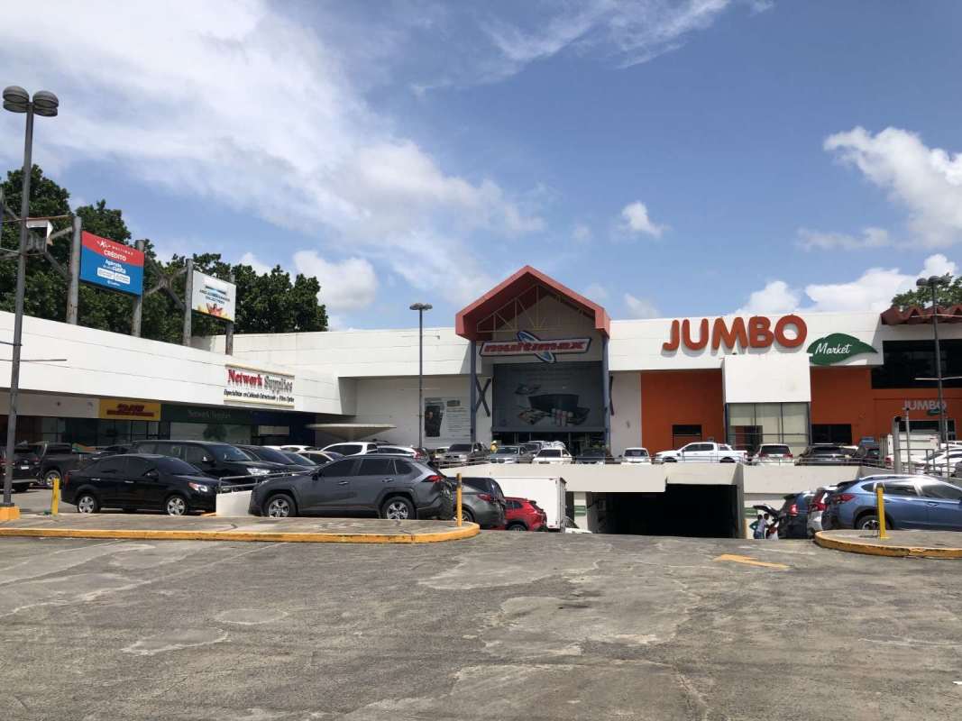 Exterior of shopping plaza with parking lot and store signs including supermarket Jumbo Market in Plaza El Cohete Panama City