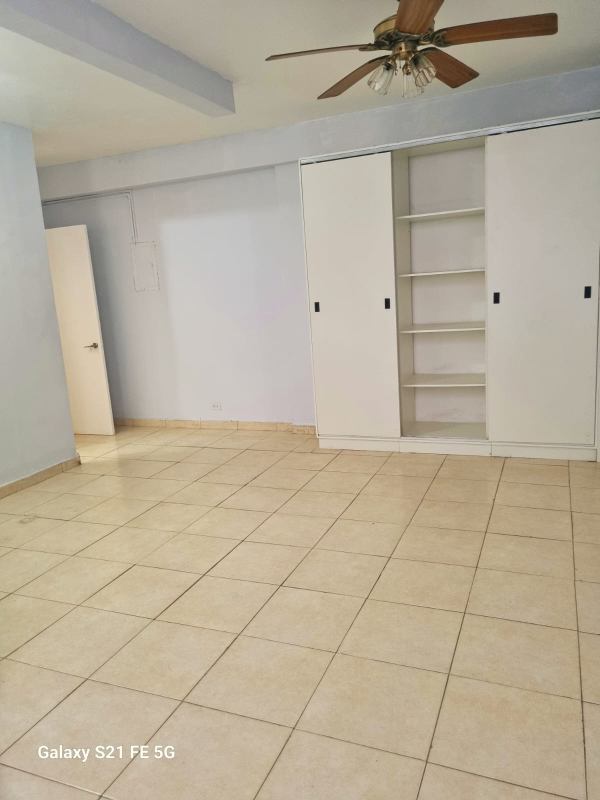 Spacious bedroom with built-in closet, beige tiled floor and ceiling fan in Panama apartment