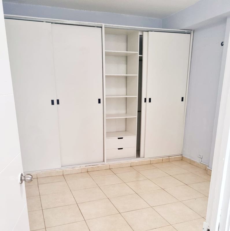 Bedroom with wardrobe, white sliding doors, open shelving, tile flooring in Panama apartment