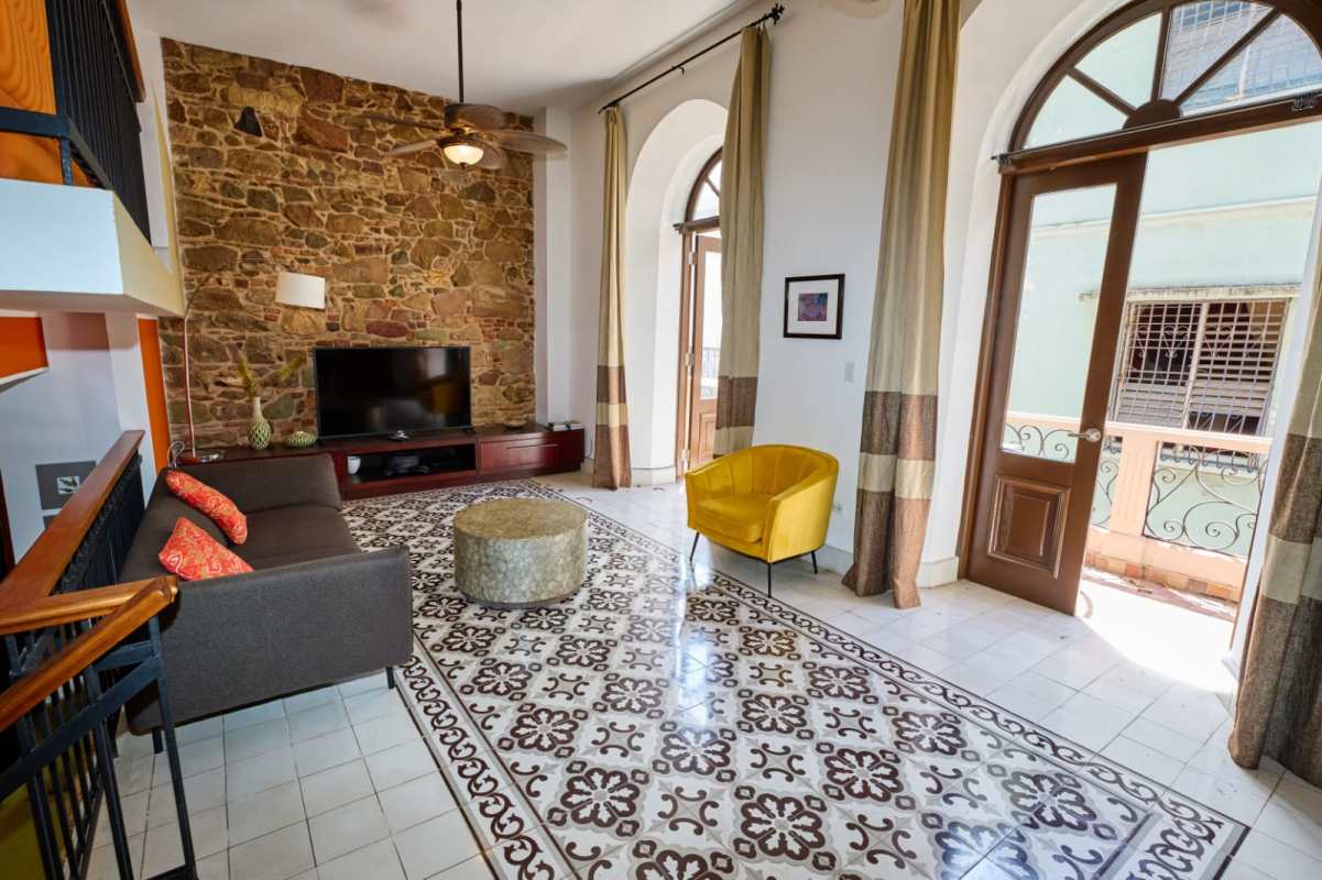 High ceiling living space with exposed stone wall, arched windows, and eclectic decor in historic Panama loft