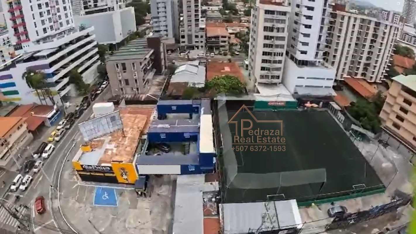 Aerial city view with commercial lot, surrounding residential towers, soccer field, and Panama skyline