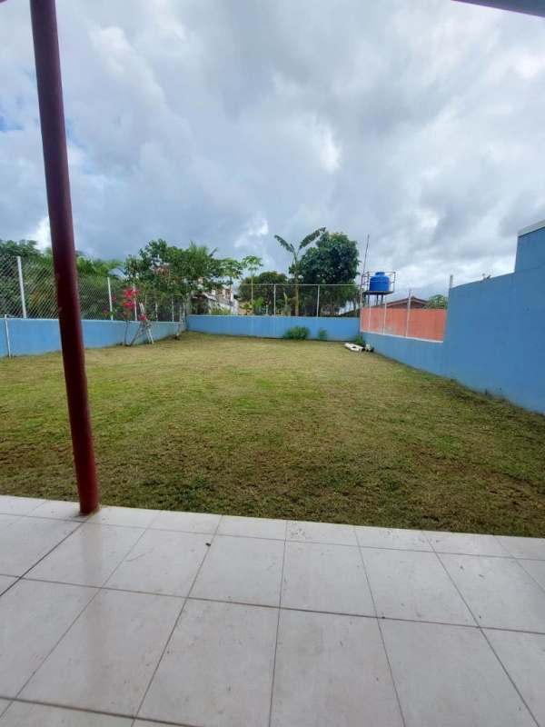 Spacious backyard with grass lawn, blue perimeter fence and covered patio at Ciudad San Lorenzo La Cabima