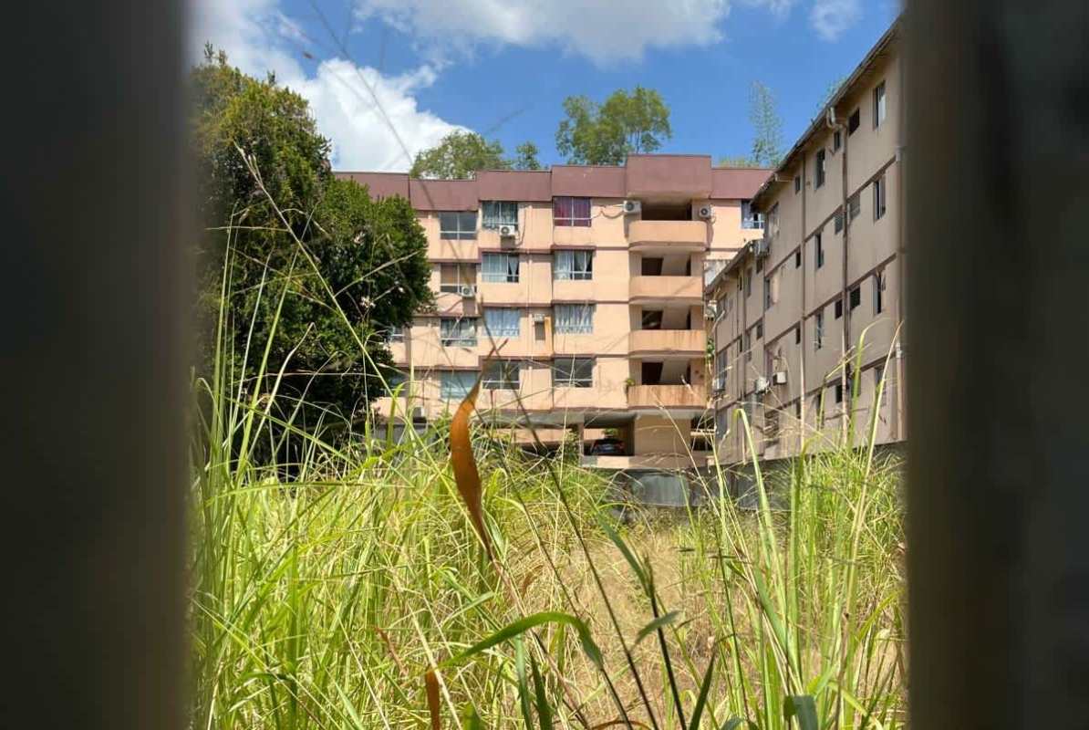 Multi-story beige apartment buildings with balconies behind grassy vacant lot Panama City