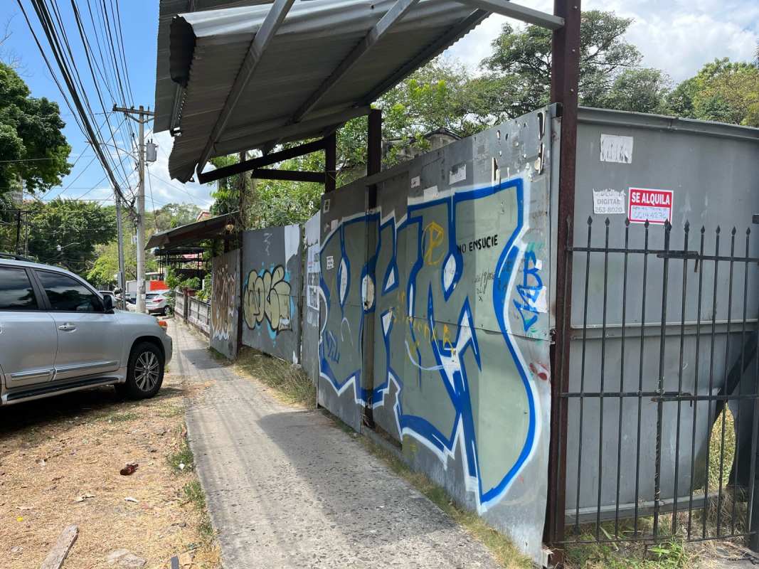Metal fence surrounds vacant commercial lot with sidewalk near major Panama City institutions