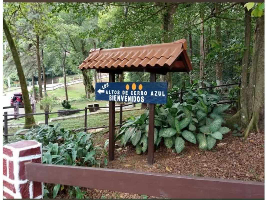 Rustic wooden gated entrance with tiled roof surrounded by lush greenery in Altos de Cerro Azul
