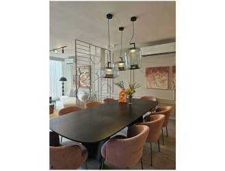 Open concept dining room with dark table, pink chairs, pendant lighting and wall art at Alere new home Panama Pacifico