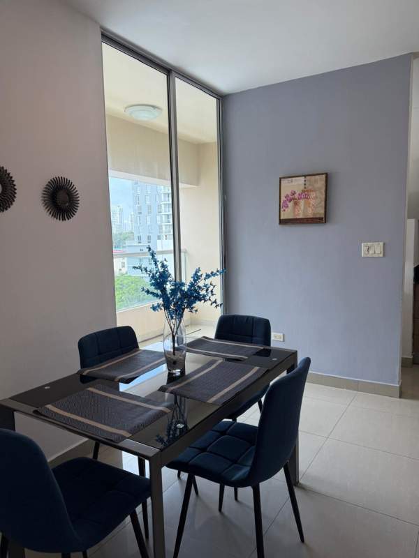 Bright dining room with glass table, blue chairs, large window city view, apartment rental Panama City