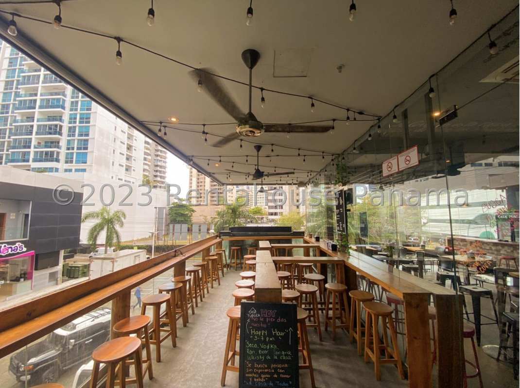 Covered outdoor bar terrace with city views, string lighting and wooden furniture at Balboa Boutiques Panama