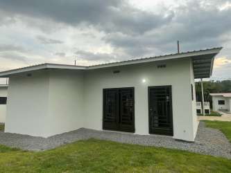 Exterior minimalist single-story home with gravel path, yard, and security bars in Bariloche Dolega