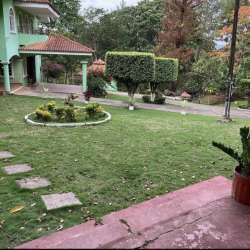 Green house with manicured lawn, decorative garden bed, carport and paved driveway in Capira countryside