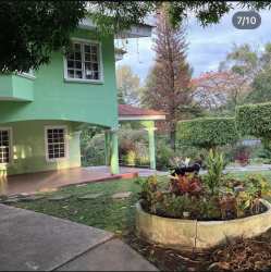 Green two-story house with covered porch and landscaped garden at estate for sale Panama