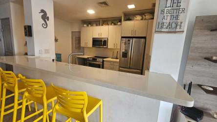 Remodeled kitchen with Italian cabinets, stainless appliances, quartz countertop, yellow bar stools at Playa La Barqueta condo Chiriquí Panama